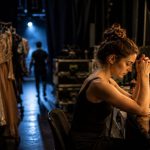 Artiste en préparation dans une loge de théâtre, entourée de costumes de scène et concentrée sur son rituel avant l'entrée en spectacle