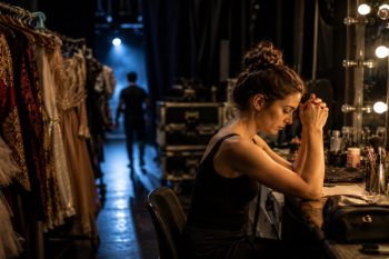 Artiste en préparation dans une loge de théâtre, entourée de costumes de scène et concentrée sur son rituel avant l'entrée en spectacle
