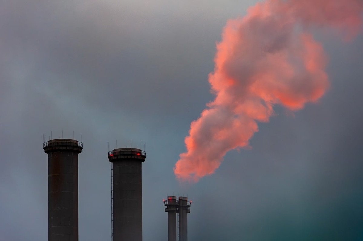Trois cheminées industrielles émettent une fumée rose pâle dans un ciel gris Trois cheminées industrielles émettent une fumée rose pâle dans un ciel gris