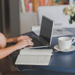 Une femme travaille sur ordinateur portable avec cahier et tasse de café
