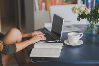 Une femme travaille sur ordinateur portable avec cahier et tasse de café