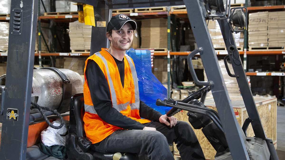 Un salarié souriant pilote un chariot élévateur en entrepôt Un salarié souriant pilote un chariot élévateur en entrepôt